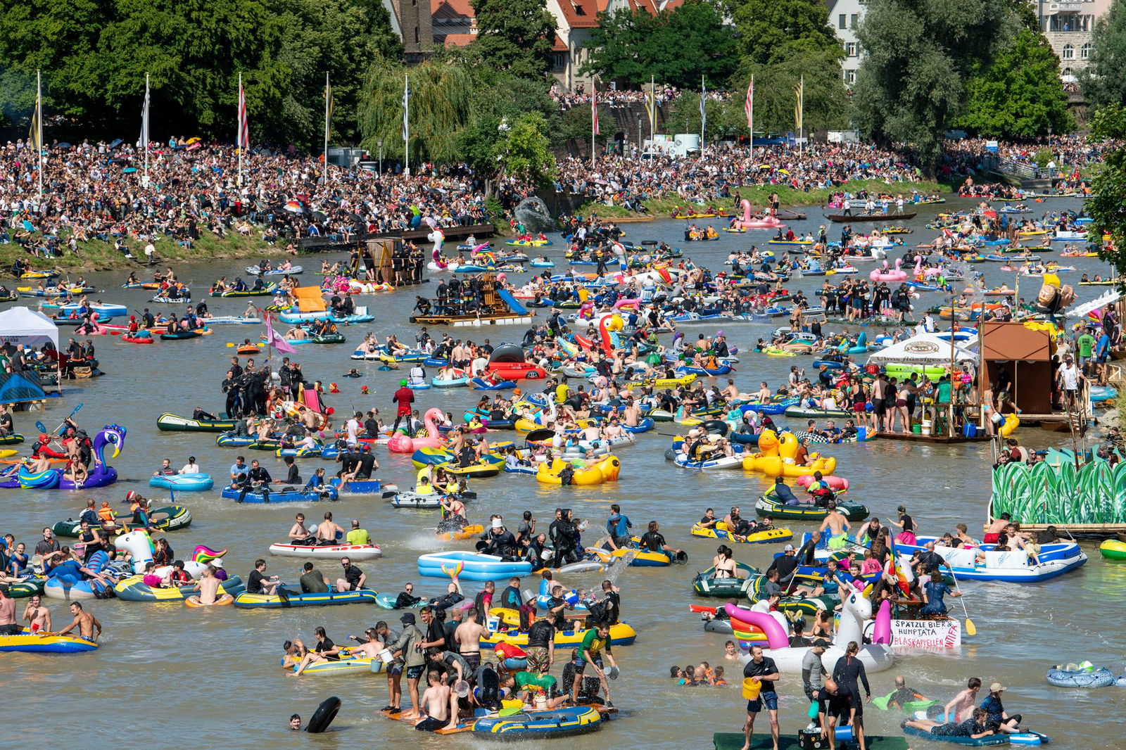 Unzählige Schlauchboote treiben den Fluss hinab, während noch mehr Schaulustige entlang des Ufers mitfeiern.