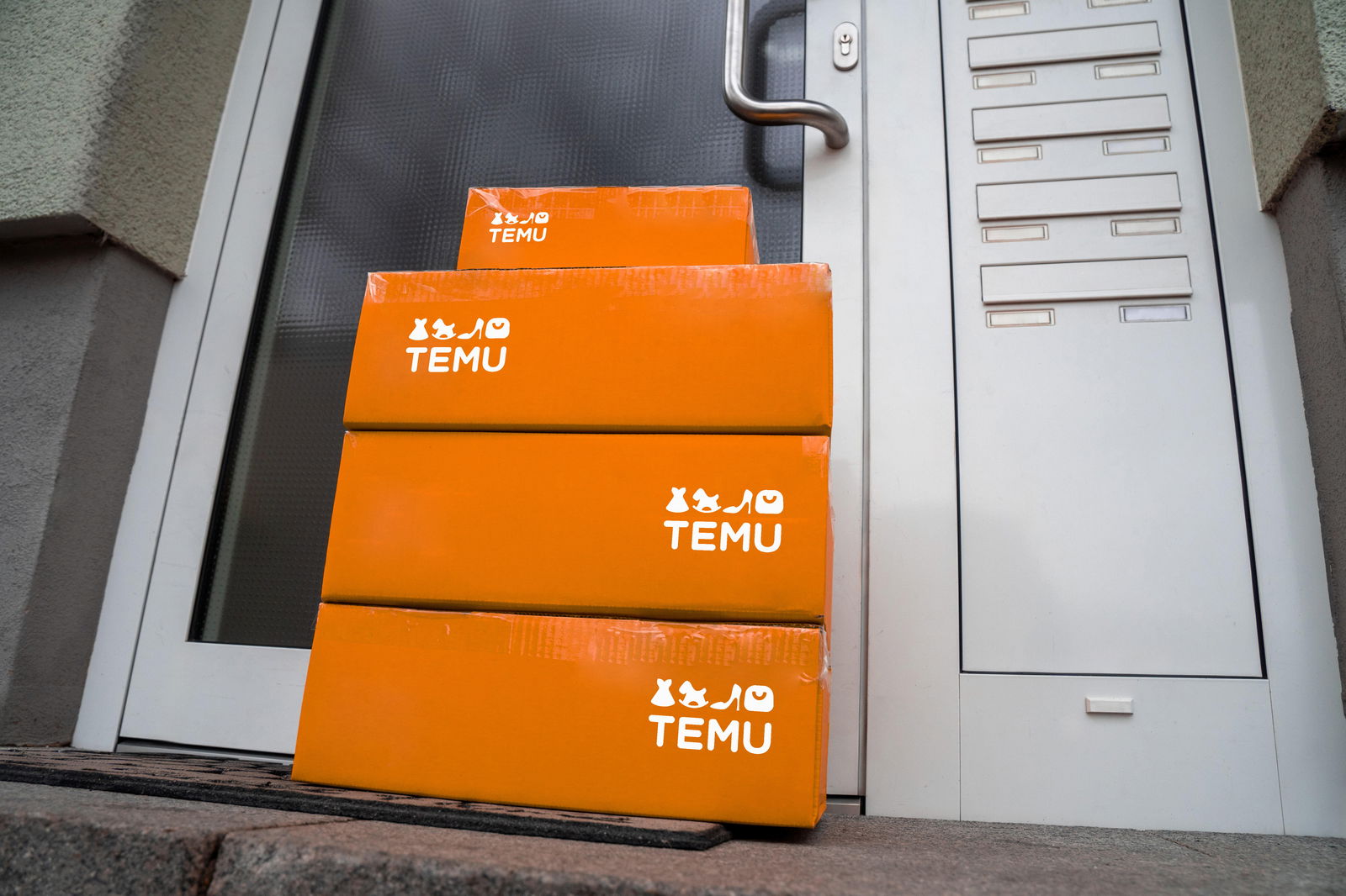 Symbolbild: Orangefarbene Temu-Pakete vor einer Haustür verdeutlichen den Boom von internationalen E-Commerce-Plattformen. Temu, bekannt für günstige Preise und große Produkt-Auswahl, aggressive Marketingstrategien in Europa und den USA.