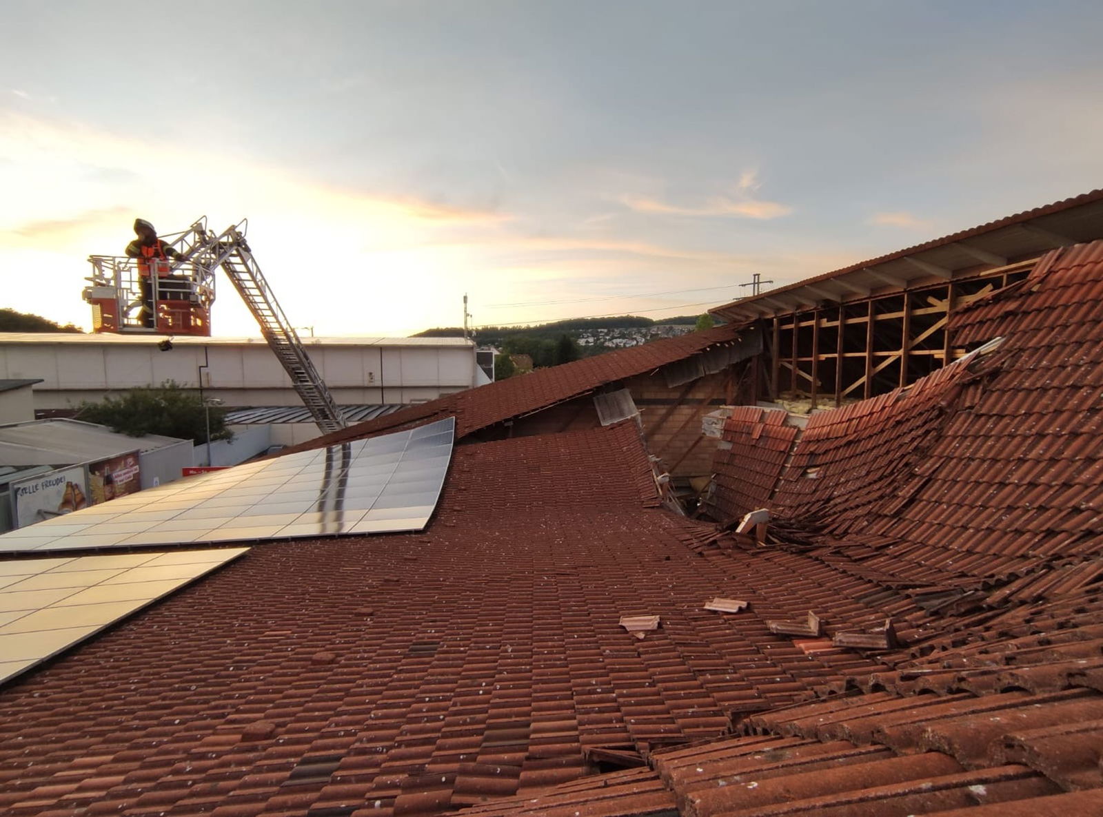 Vom Korb einer Drehleiter heraus kontrolliert ein Feuerwehrmann den eingestürzten Dachbereich.