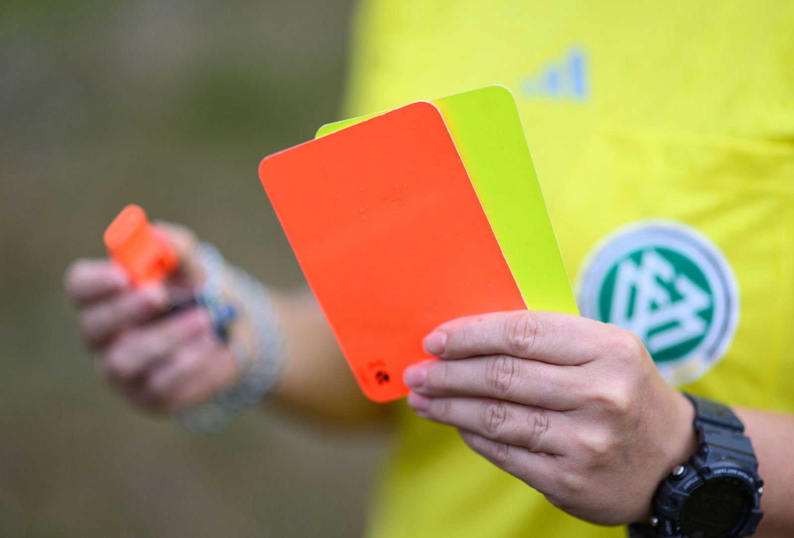 Schiedsrichterin mit rot-gelber Karte in der Hand und Trillerpfeife