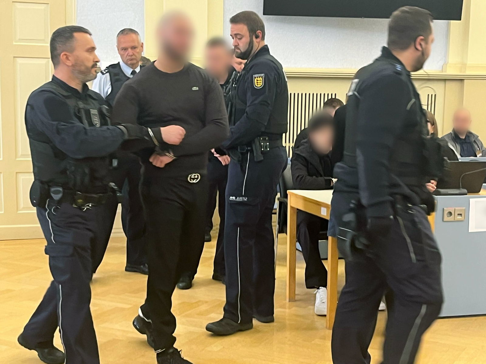 Einer der Angeklagten wird in Handschellen in den Gerichtssaal geführt. 