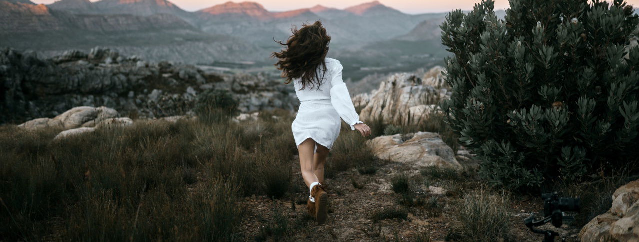 Frau in weißem Kleid rennt durch Berglandschaft