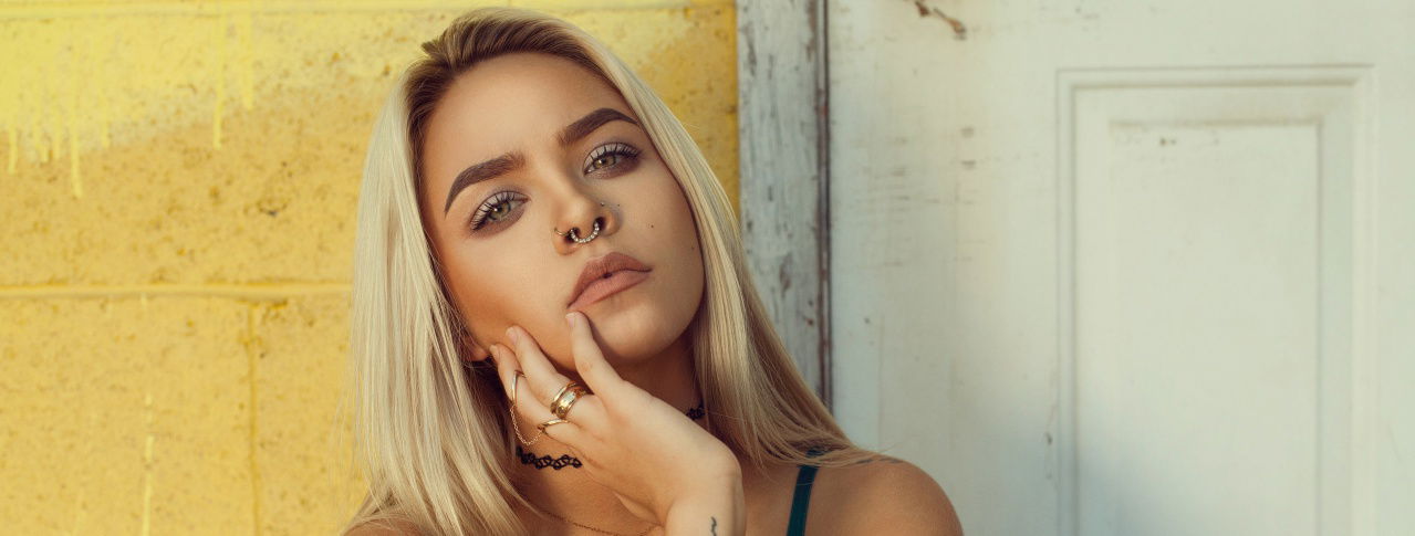 Frau mit blonden Haaren hält sich die Hand ans Kinn