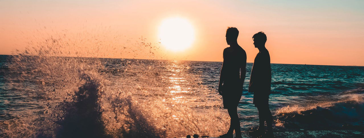Zwei Männer stehen am Meer und sehen den Sonnenuntergang