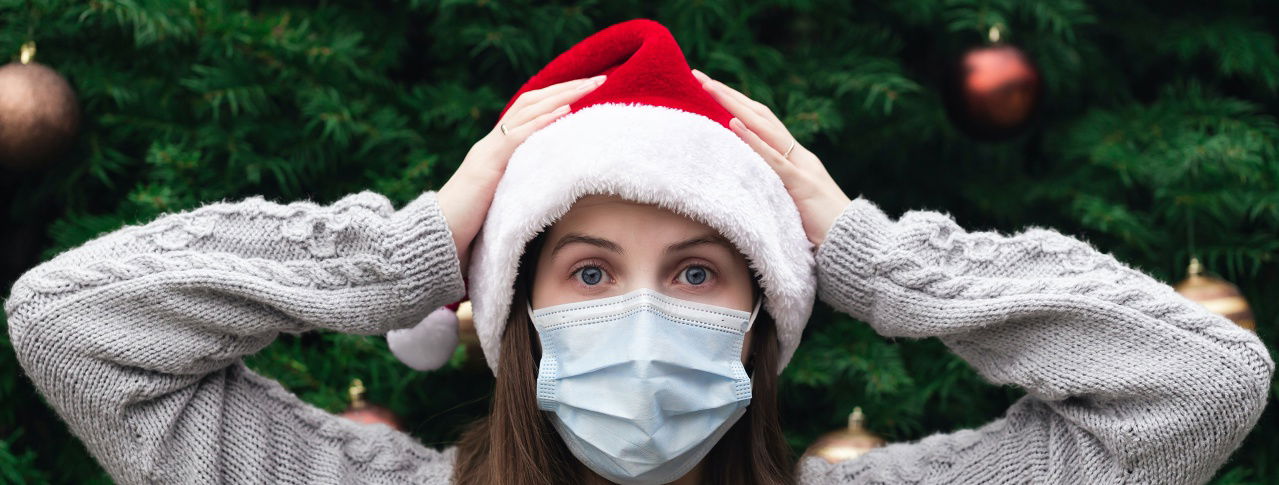 Frau mit grauem Pulli, Maske und einer Weihnachtsmütze hebt sich die Hände an den Kopf 