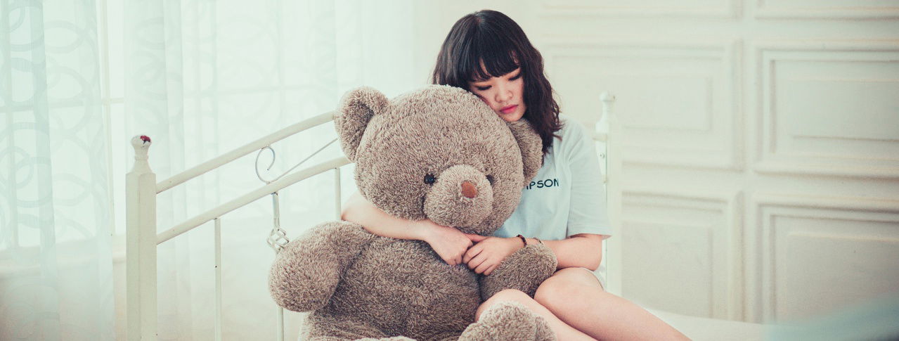 Frau sitzt auf Bett und umarmt Teddybär