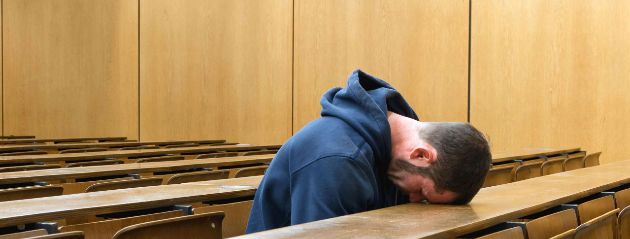Mann legt Kopf auf Tisch im Vorlesungssaal