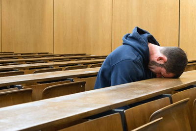 Mann legt Kopf auf Tisch im Vorlesungssaal