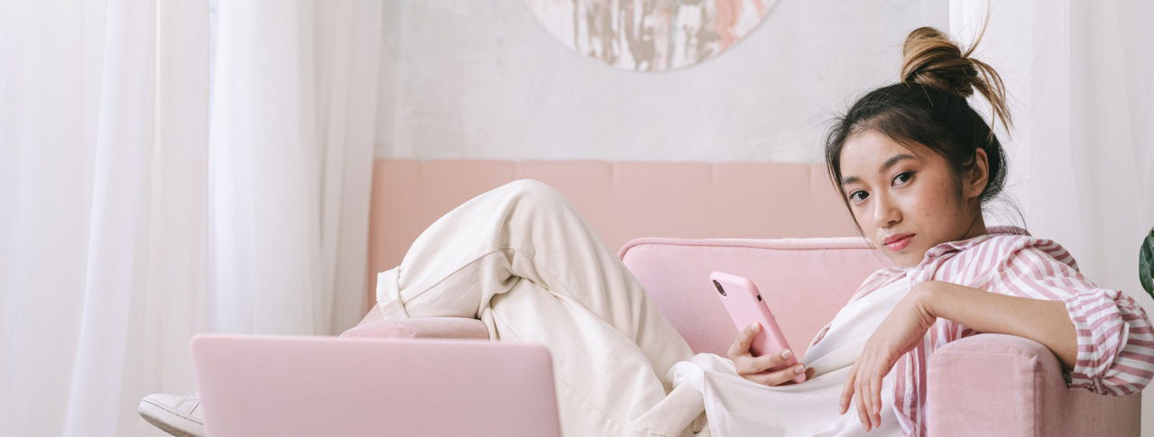 Mädchen chillt mit dem Handy auf einem rosanem Sofa