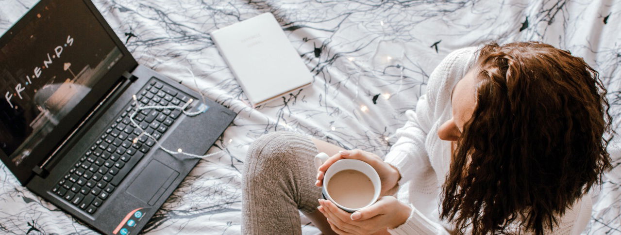 Frau mit Kaffeetasse und Computer im Bett