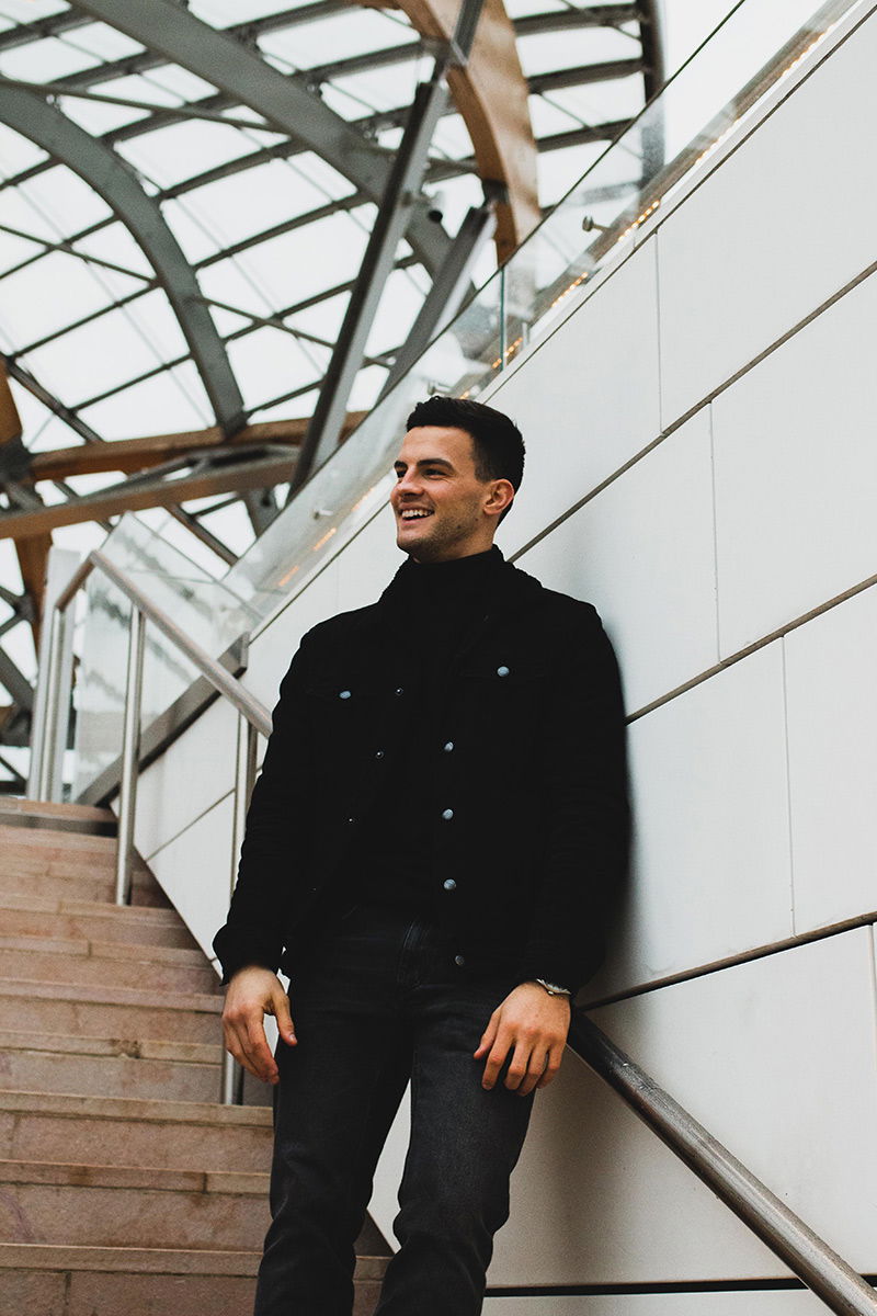 Mann steht an einer Treppe, lehnt sich an und lächelt dabei