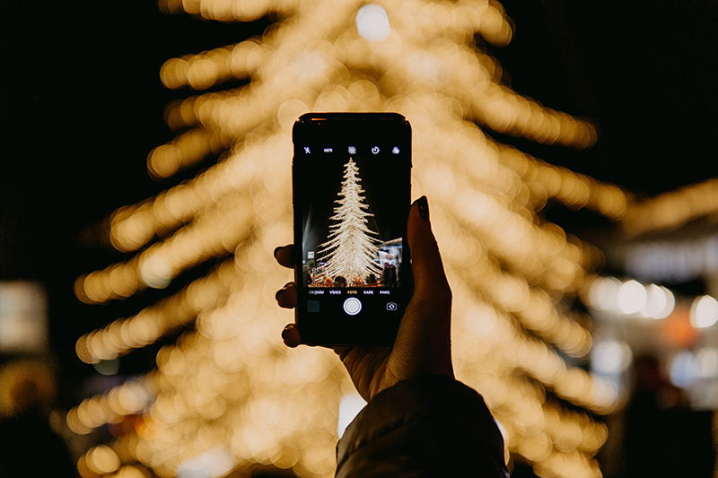 Schön beleuchteter Weihnachtsbaum wird mit einem Handy fotografiert 