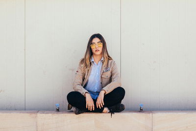 Frau mit Sonnenbrille sitzt im Schneidersitz auf einer Mauer