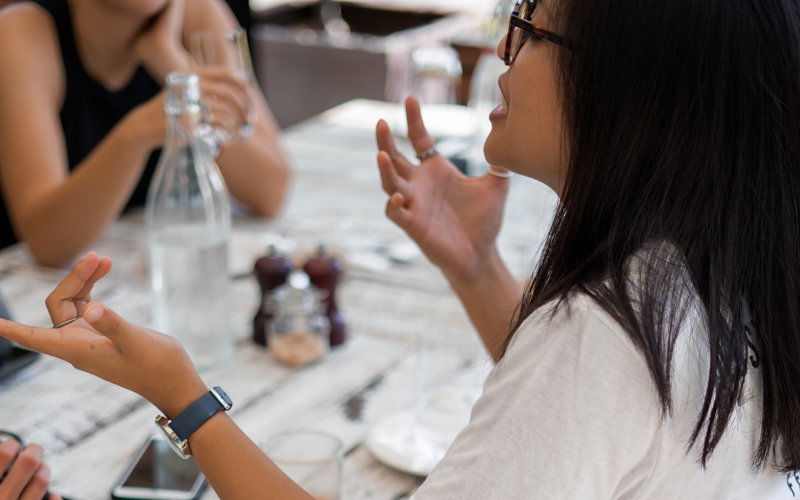 Frau sitzt an Tisch und streitet mit anderen Menschen