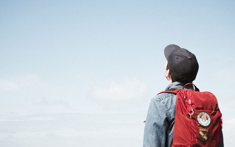 Mann mit schwarzer Kappe und rotem Rucksack schaut in den Himmel