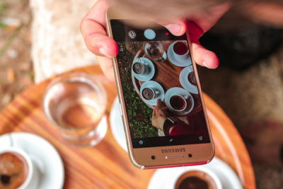 Handy wird gehalten und macht Foto von Tassen auf Tisch