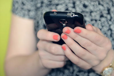 Frau mit hell rosanen Nägeln ist am Handy 