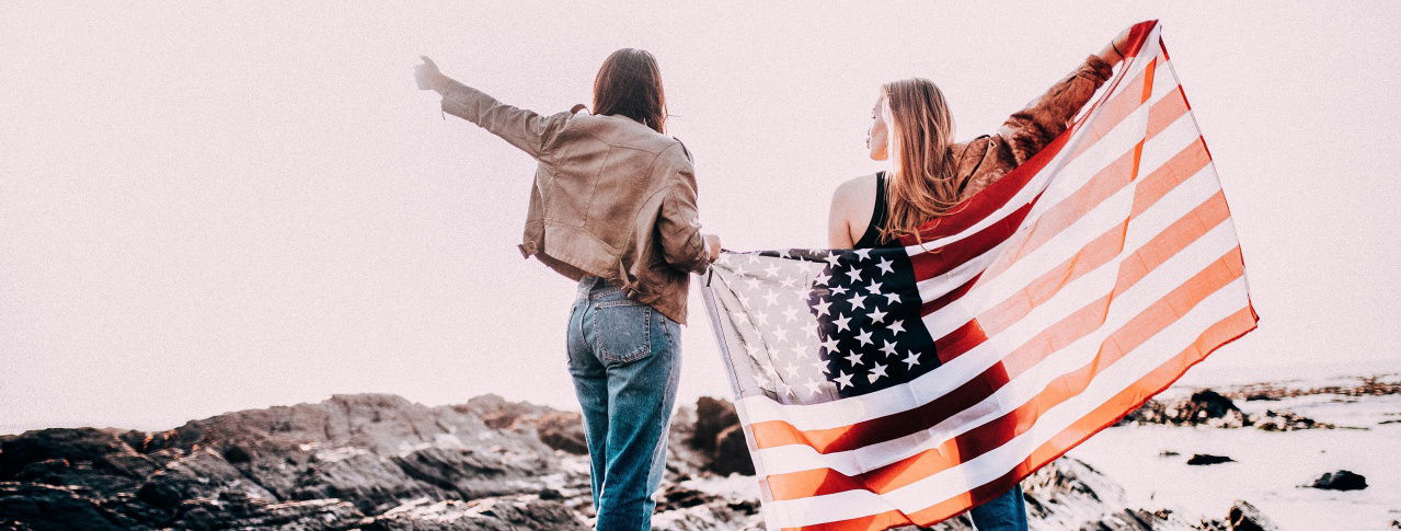 Zwei Frauen stehen an einer Klippe am Meer und haben eine USA Flagge hinter sich