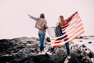 Zwei Frauen stehen an einer Klippe am Meer und haben eine USA Flagge hinter sich