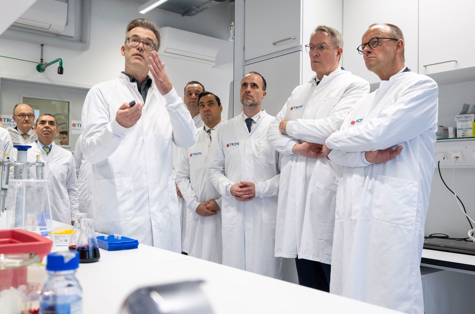 Kanzler Merz, Ministerpräsident Schweitzer und der rheinland-pfälzische Wissenschaftsminister Hoch bekommen ein Projekt erklärt, bei dem Hefe für die Produktion von RNA genutzt werden soll. 