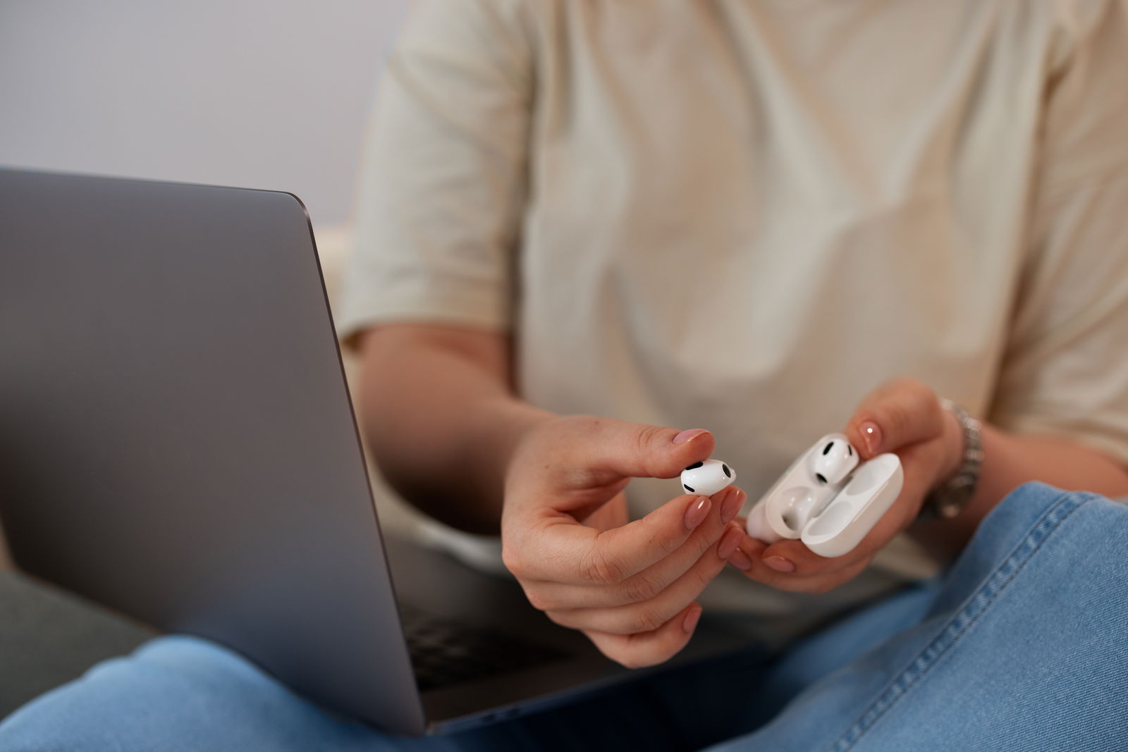 Frau hält AirPods in der Hand vor einem Laptop