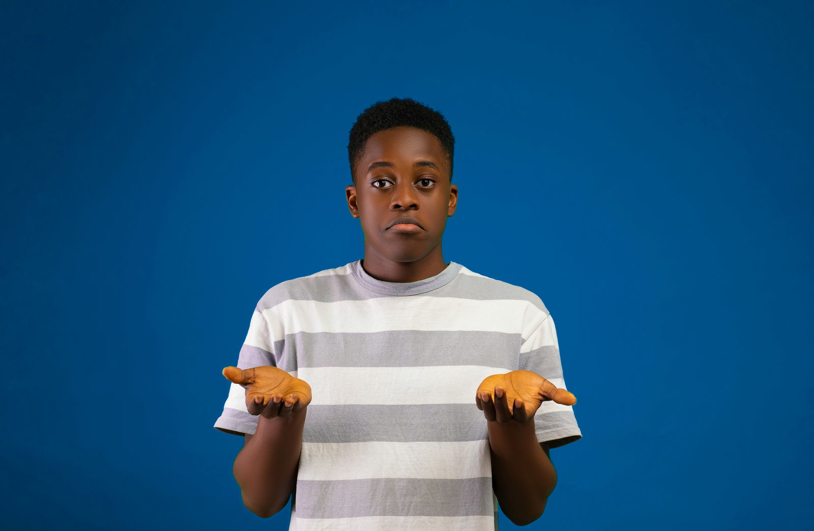 Junge vor blauem Hintergrund ist verwirrt und hebt seine Hände