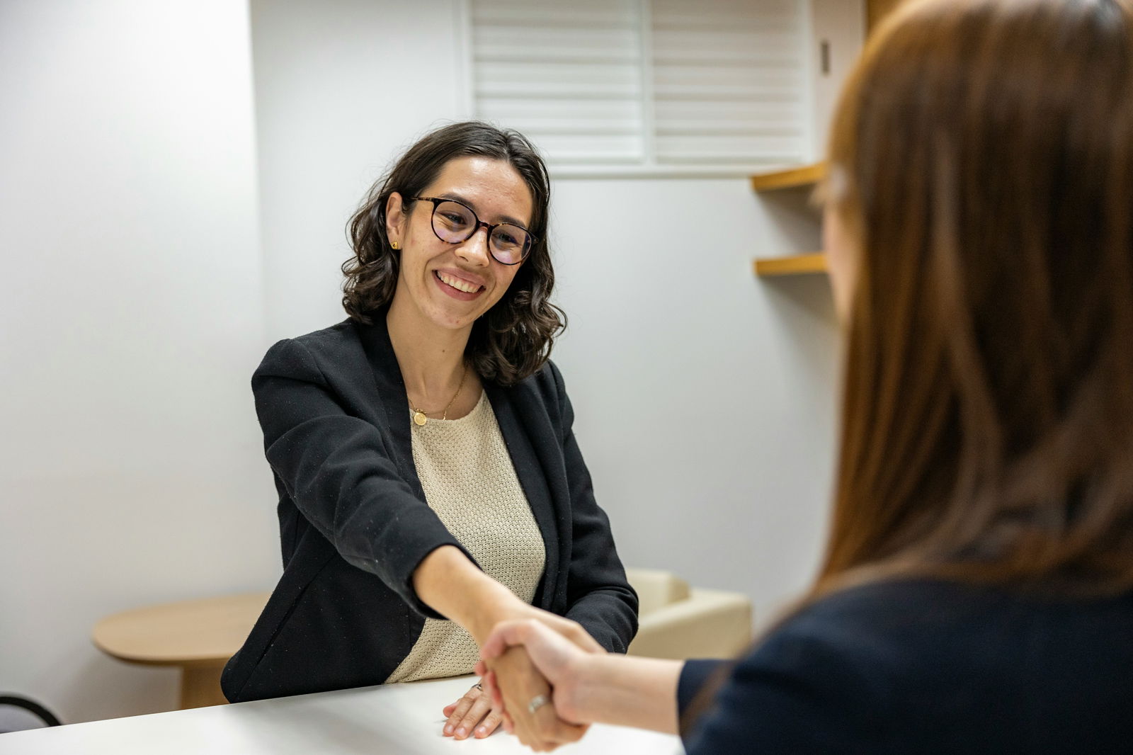 Frau mit Brille und Blazer schüttelt Hand von anderer Frau