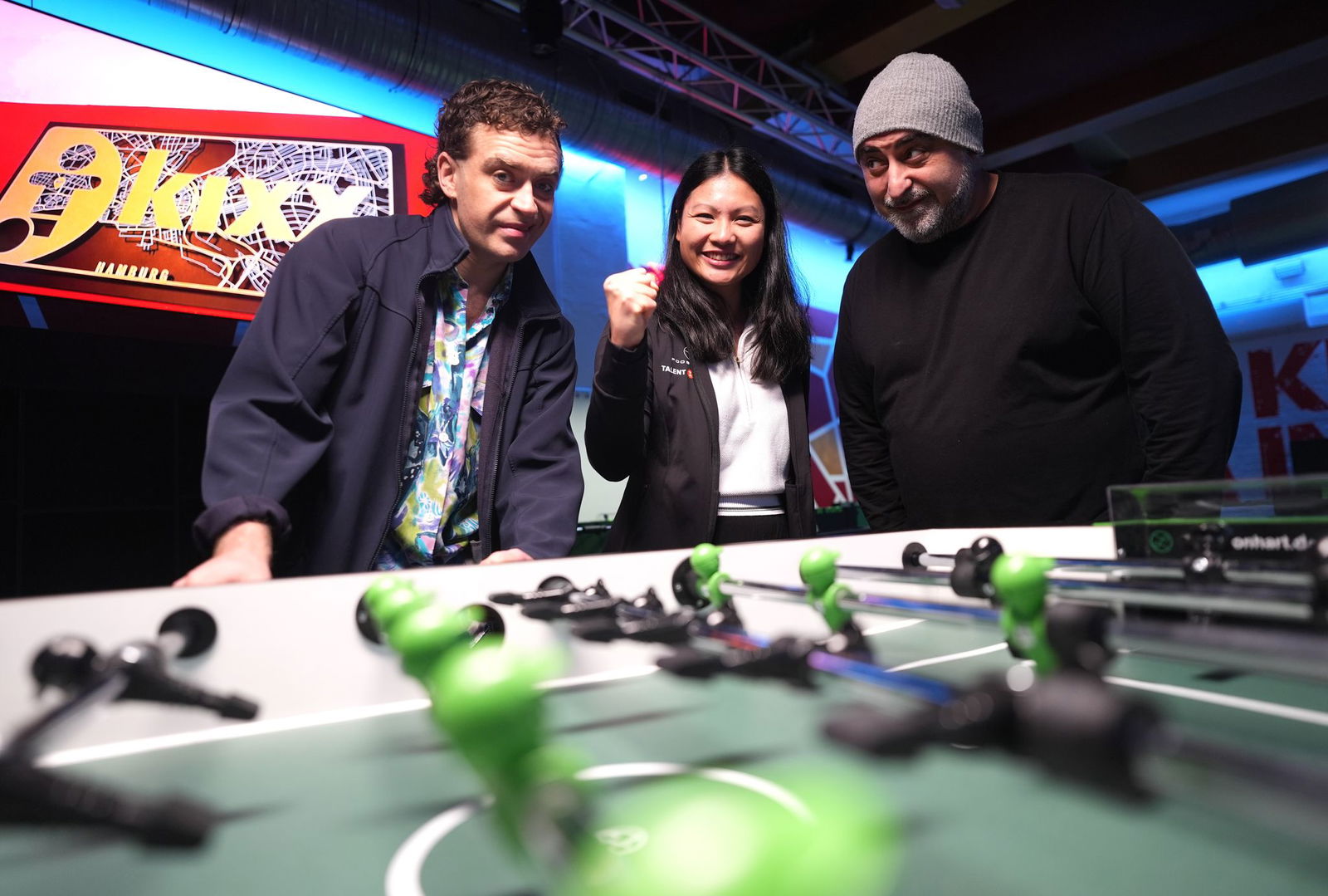 Die Großstadtrevier-Schauspieler Özgür Karadeniz und Enrique Fiß stehen neben Linh Tran, Weltmeisterin im Tischkicker.