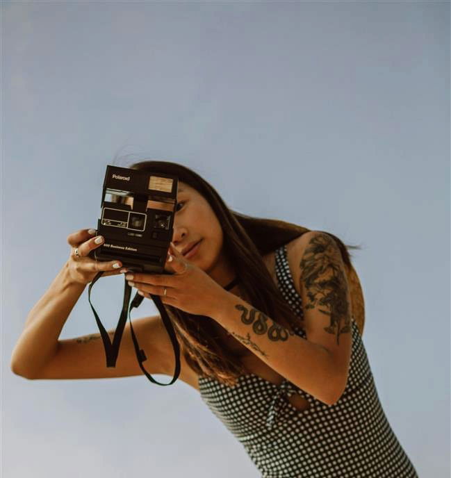 Frau hält Kamera vor blauem Himmel