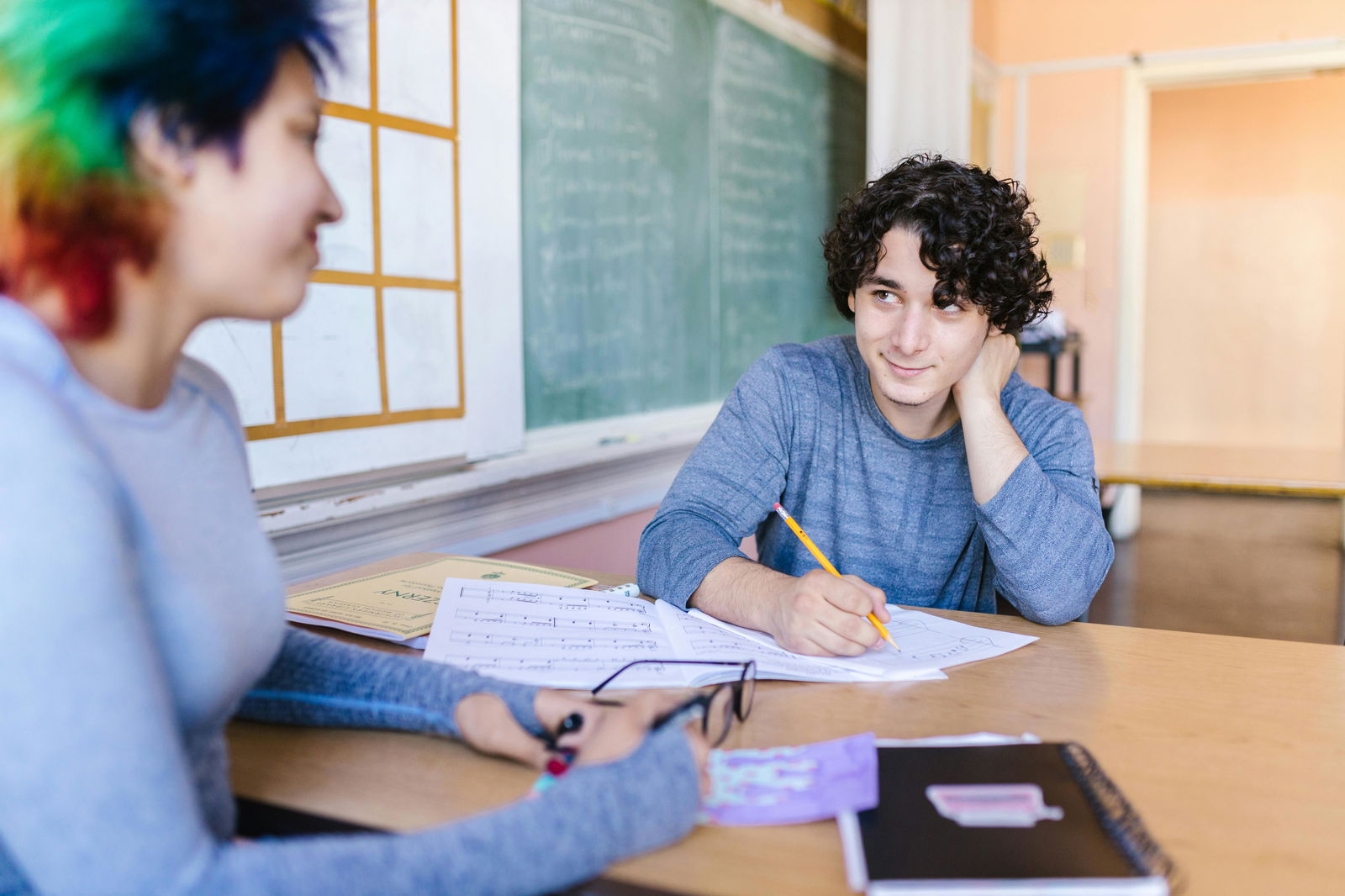 zwei Schüler schauen sich an und der eine schreibt mit Stift auf Papier