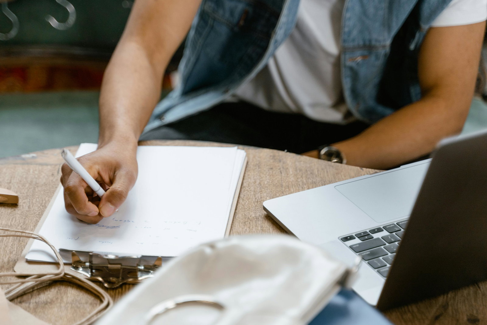 Mann sitzt an Tisch mit Laptop und schreibt auf Block