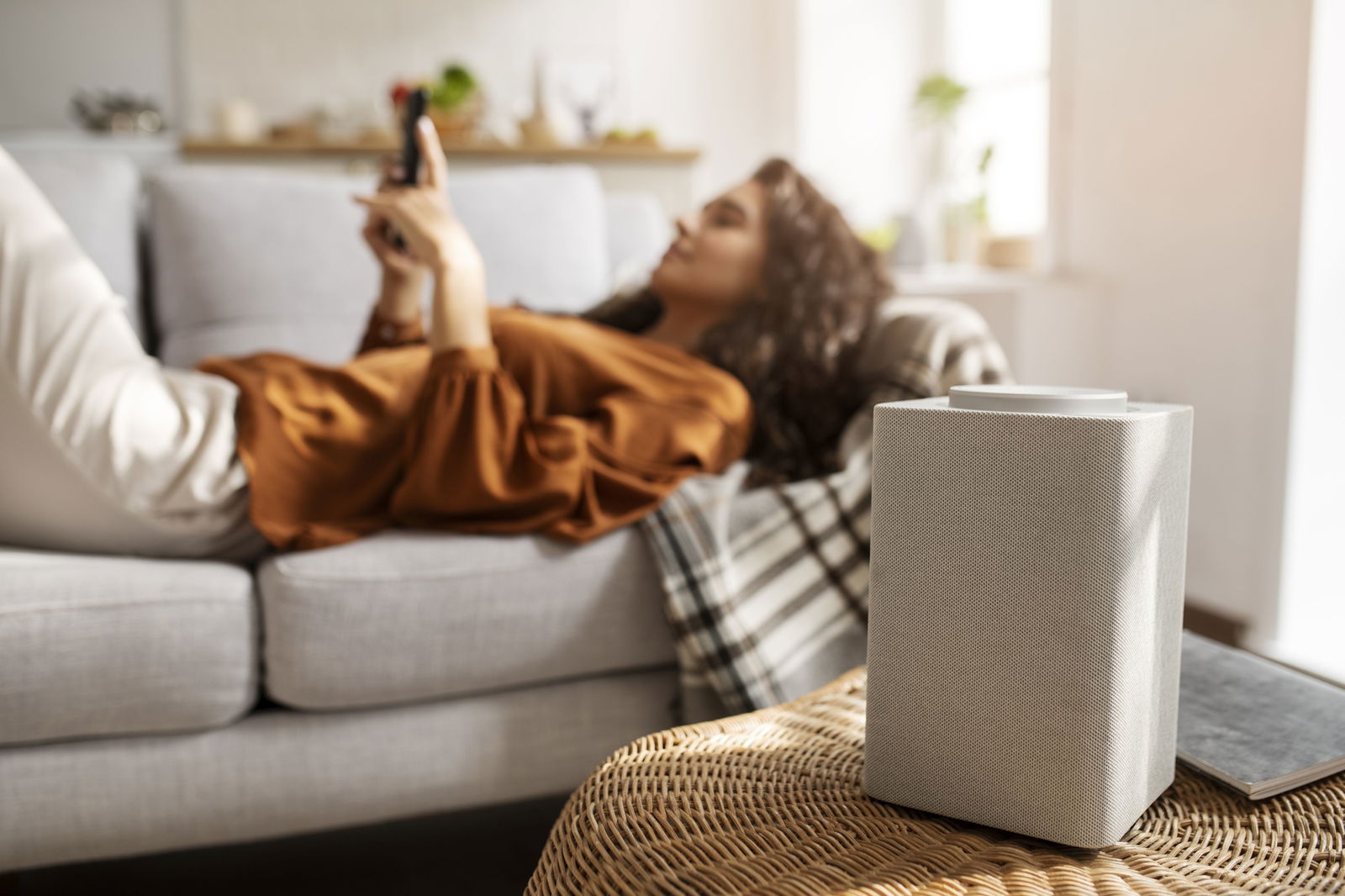 Frau liegt auf Couch, Smart Speaker im Vordergrund