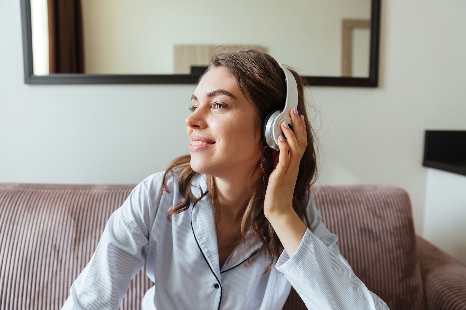 Frau im Pyjama mit Kopfhörern auf der Couch
