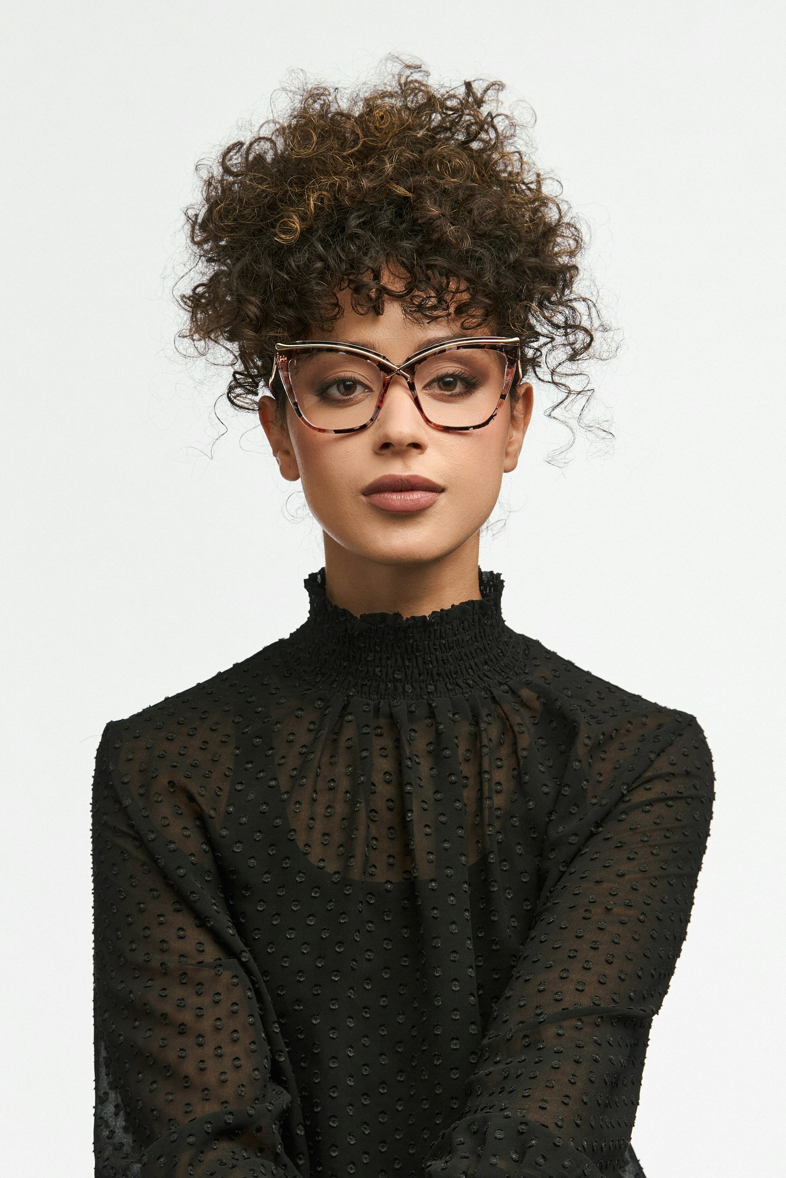 Frau mit Brille und lockigem Dutt vor weißem Hintergrund schaut in die Kamera