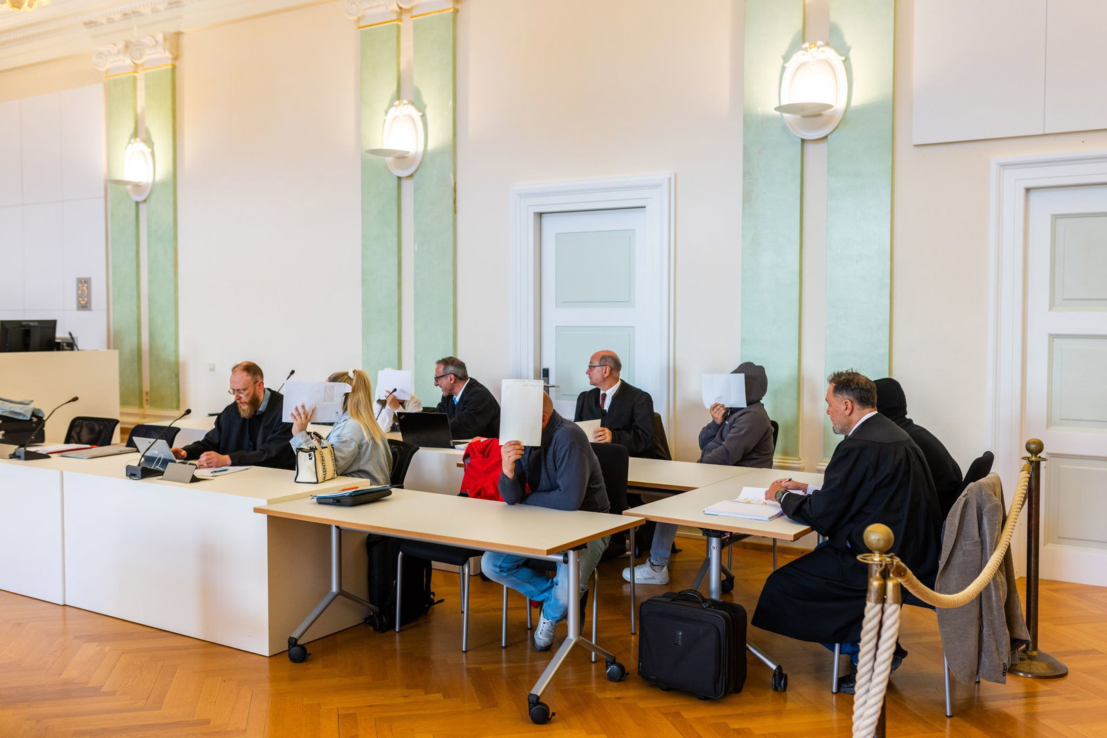 Drei Männer und zwei Frauen sitzen mit ihren Anwälten auf der Anklagebank.