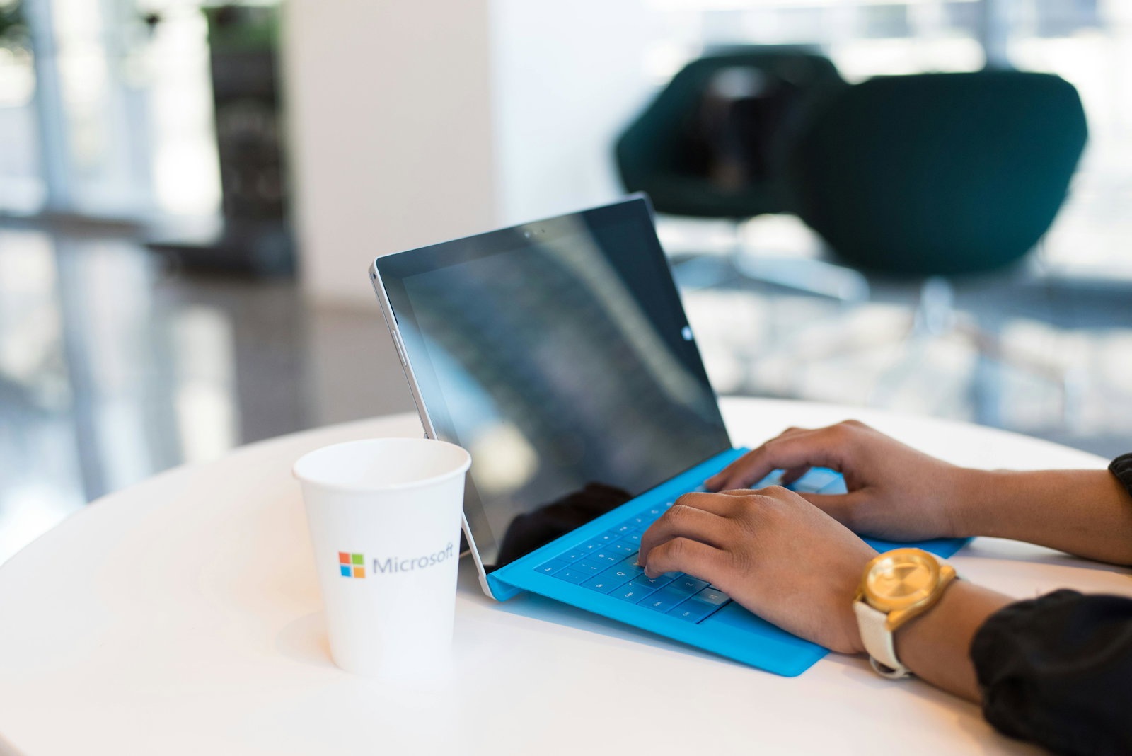 Person tippt an einem blauen Laptop daneben steht ein Becher mit dem Microsoft Logo drauf
