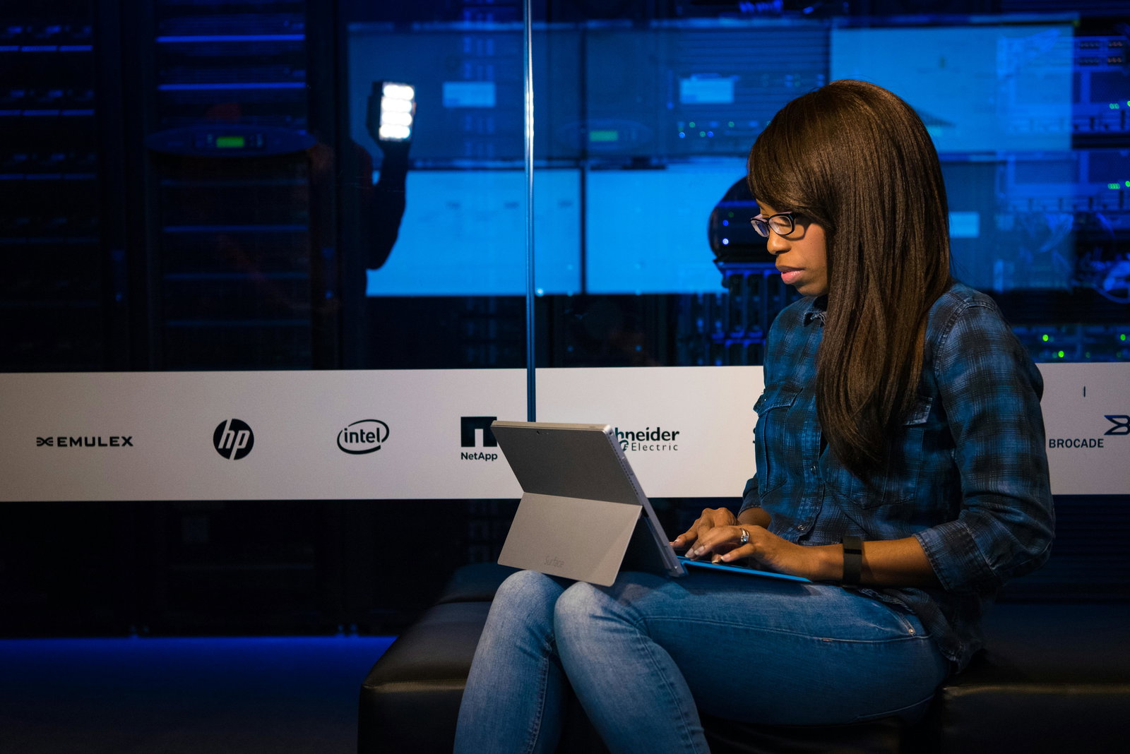 Frau mit Tablet sitzt vor blauem Datenserver 