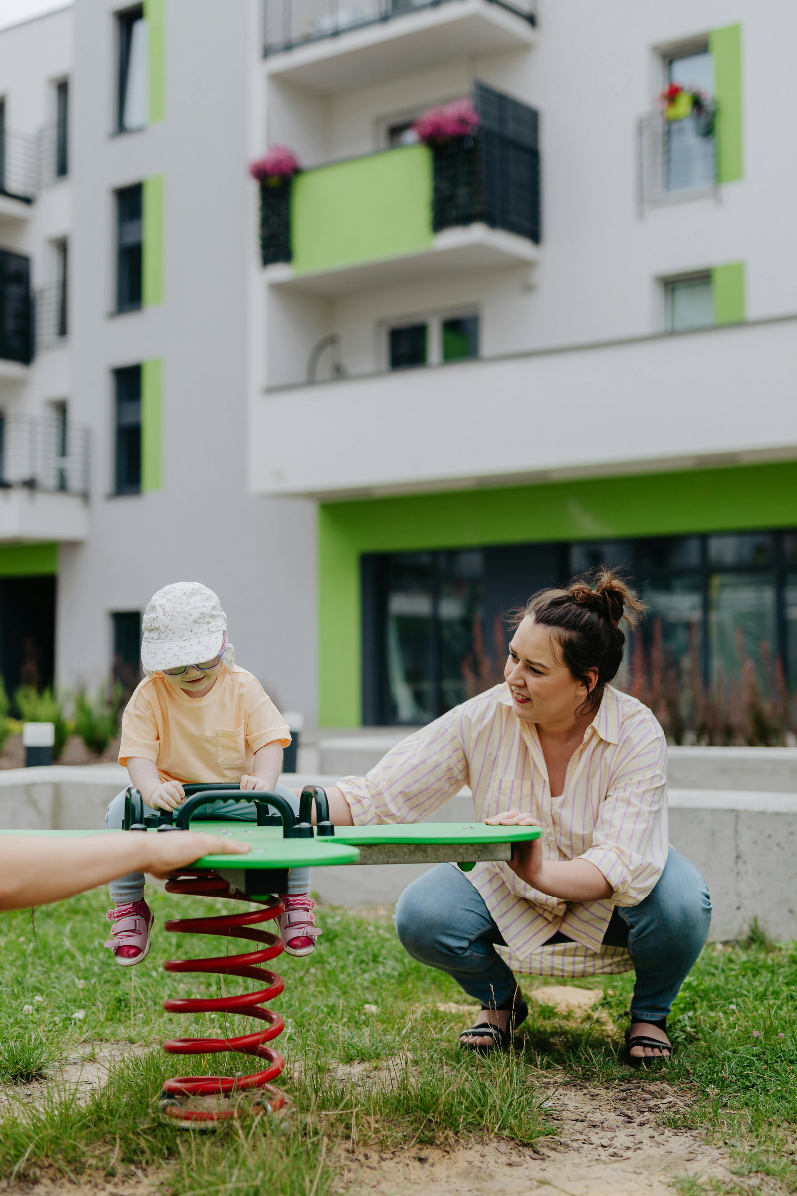 Sozialassistentin spielt mit Kind auf einer Wippe im Garten