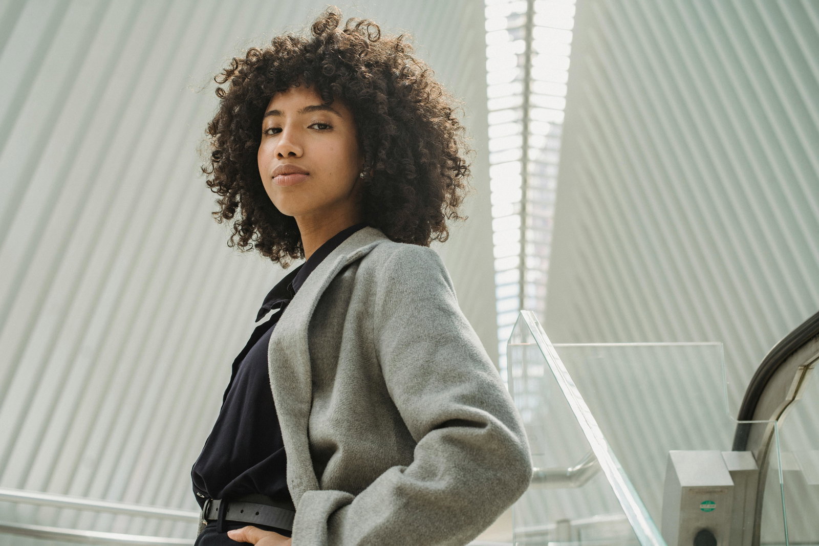 Frau mit dunklen Lockenschaut in die Kamera vor grauem Hintergrund und trägt grau