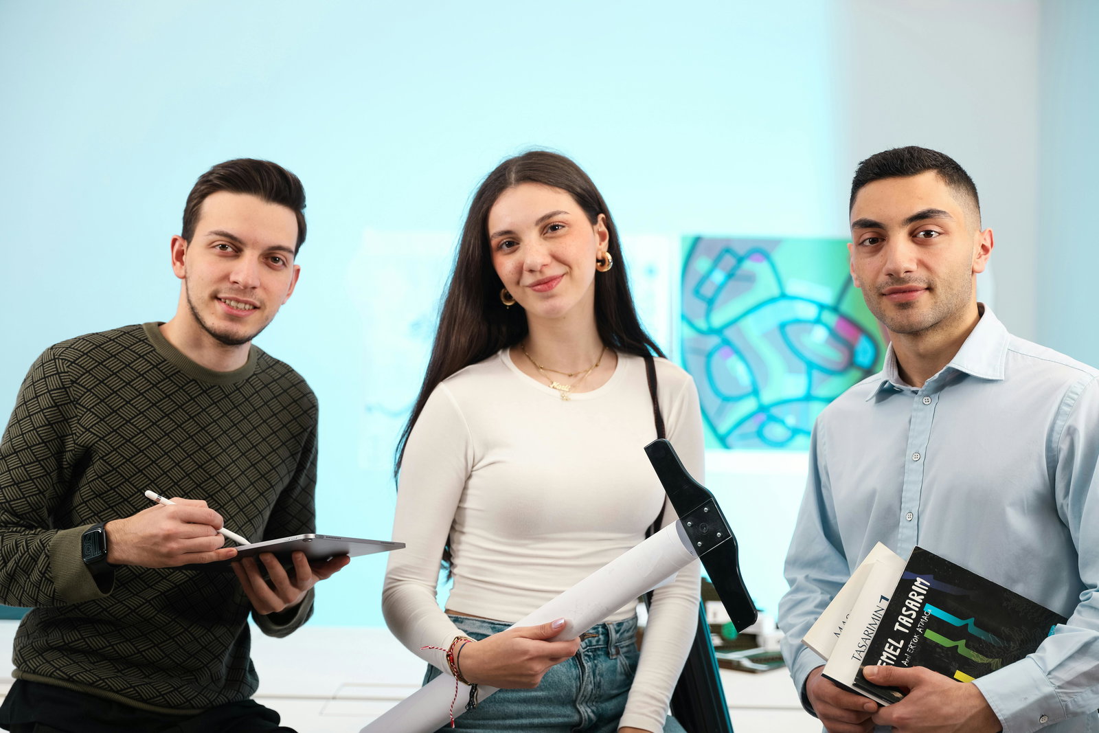 drei Personen sitzen neben einander, eine Frau in der Mitte vor hellblauem Hintergrund