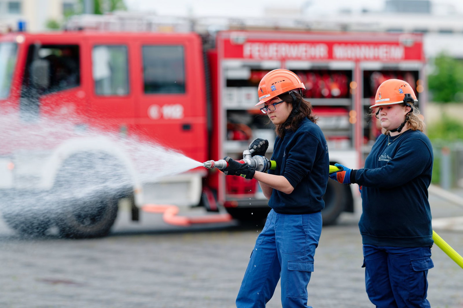 Ilias (links) und Annabella, Mitglieder der Jugendfeuerwehr in Mannheim, halten bei einer Übung einen Feuerwehrschlauch in den Händen.