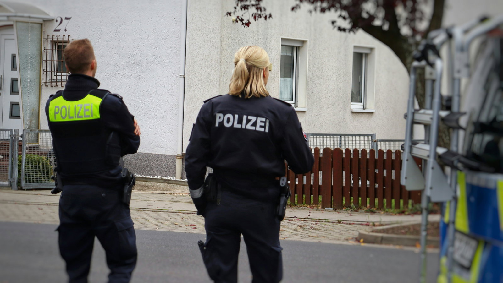 Polizistin mit kurzen Haaren steht neben Polizist an einer Straße von hinten