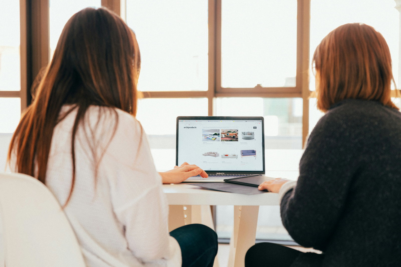 Zwei Frauen sitzen mit dem rücken zur Kamera an einem Tisch und schauen in einen Laptop