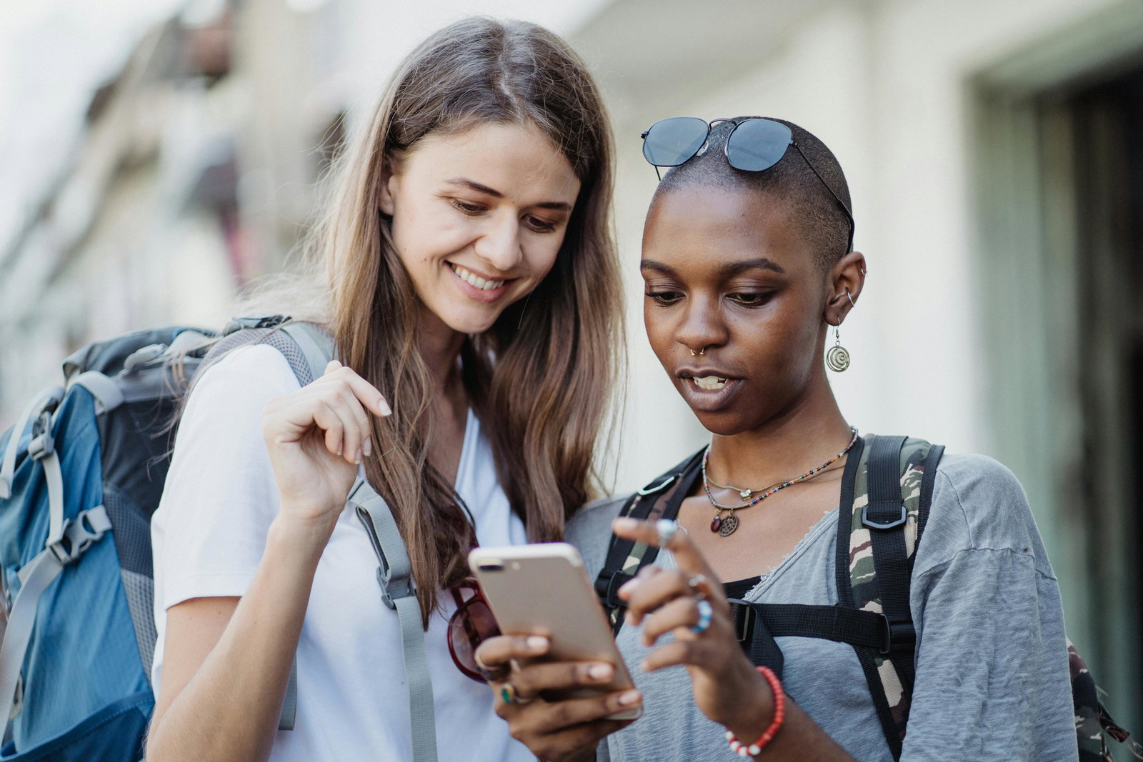 Zwei Frauen schauen auf ein Handy und reisen, sie tragen einen Rucksack