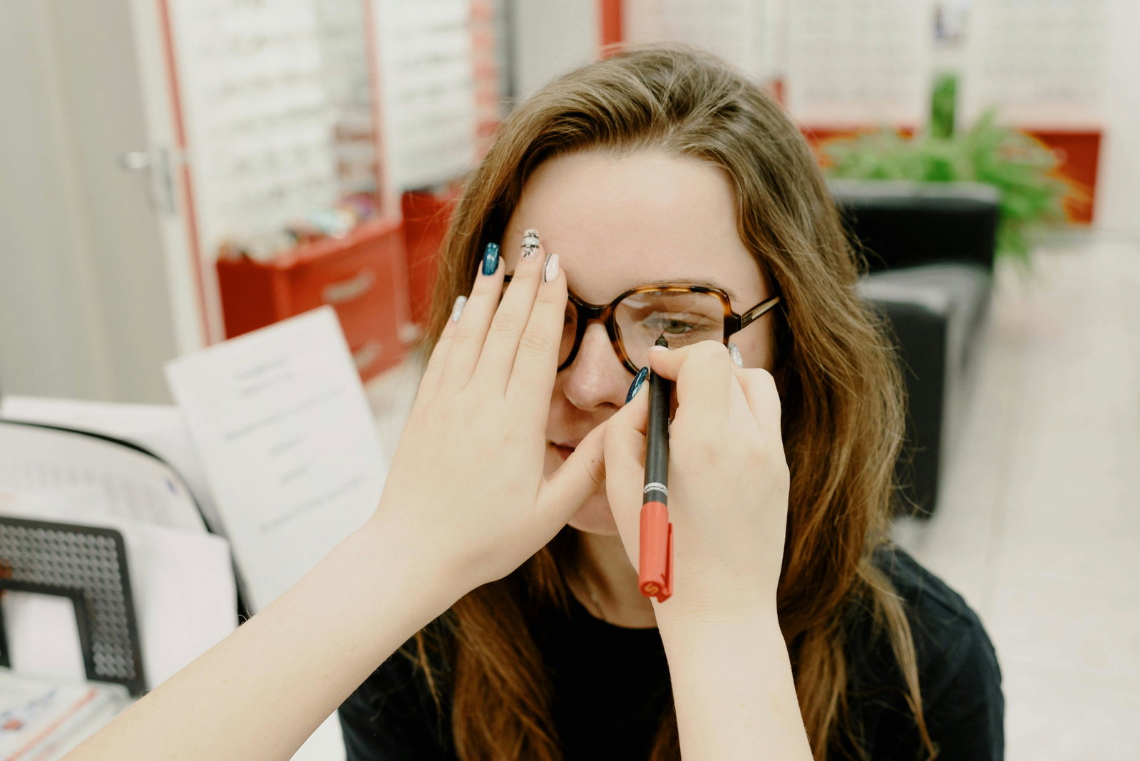 Optikerin macht Sehtest mit einer Kunden und hält ihr eine Hand vor das linke Auge
