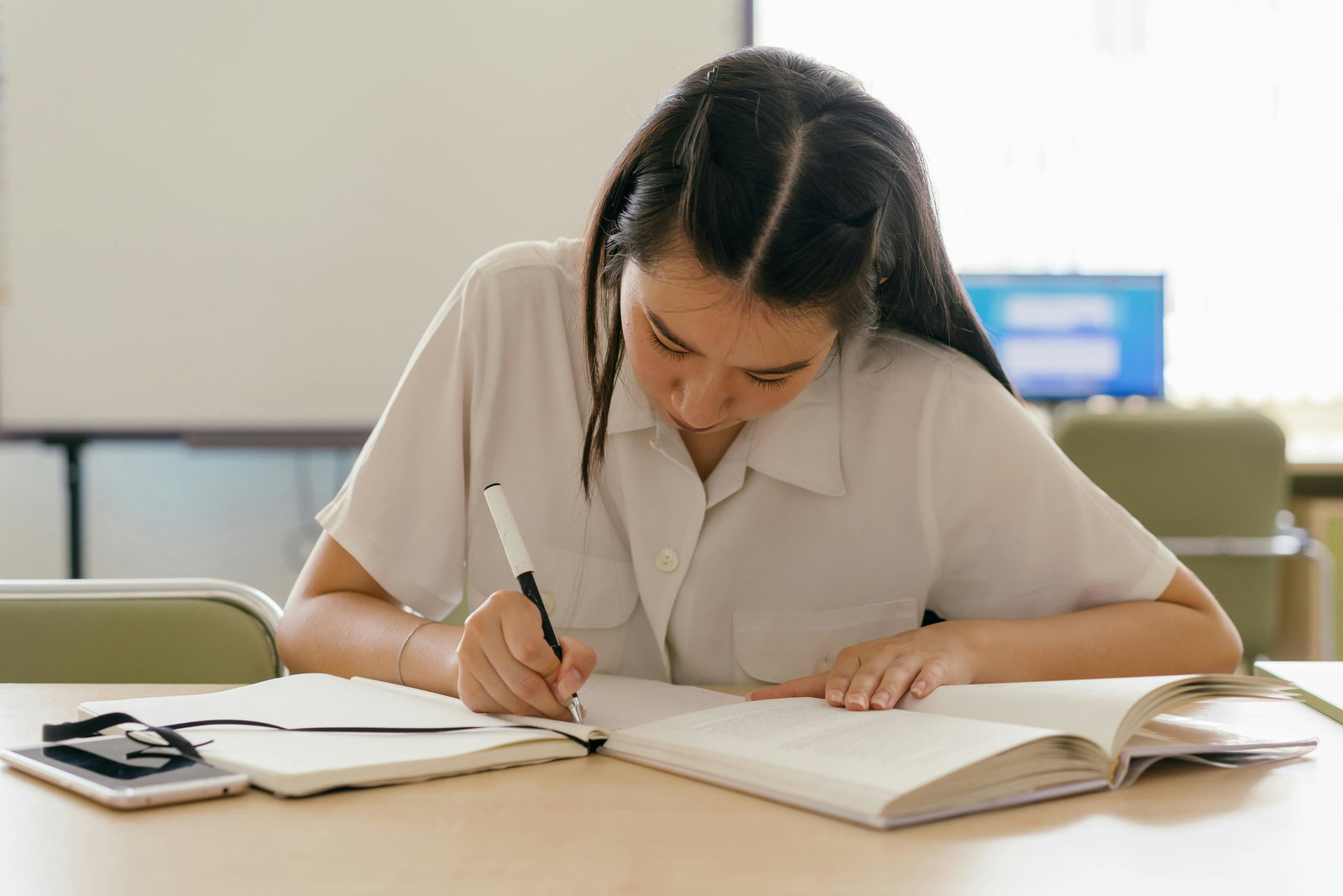 Studentin sitzt an einem Schreibtisch und schreibt auf einen Zettel