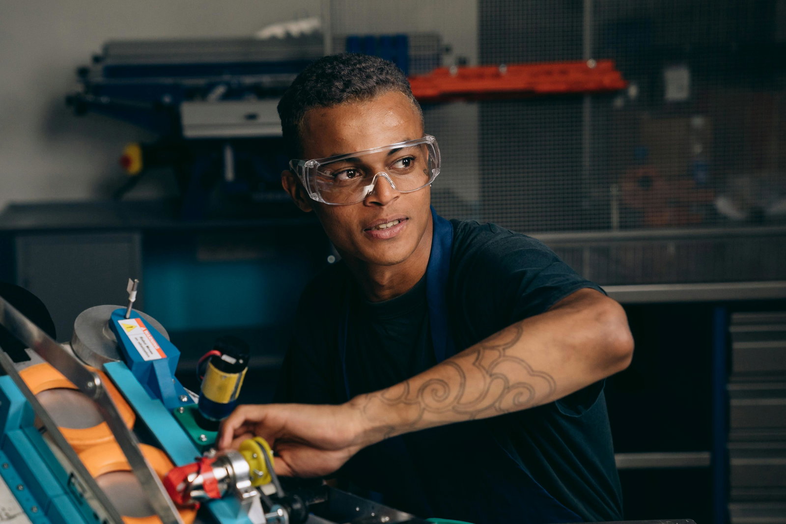Anlagenmechaniker arbeitet an einem Gerät und schaut mit Schutzbrille an Kamera vorbei