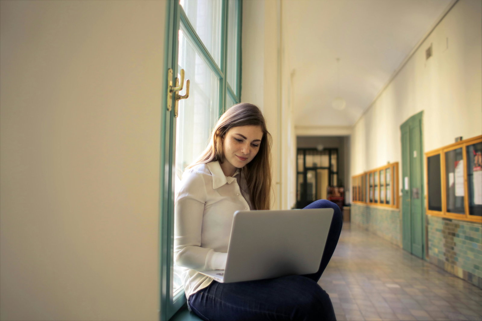 Studentin sitzt in der Uni im Flur mit ihrem Laptop und schreibt etwas