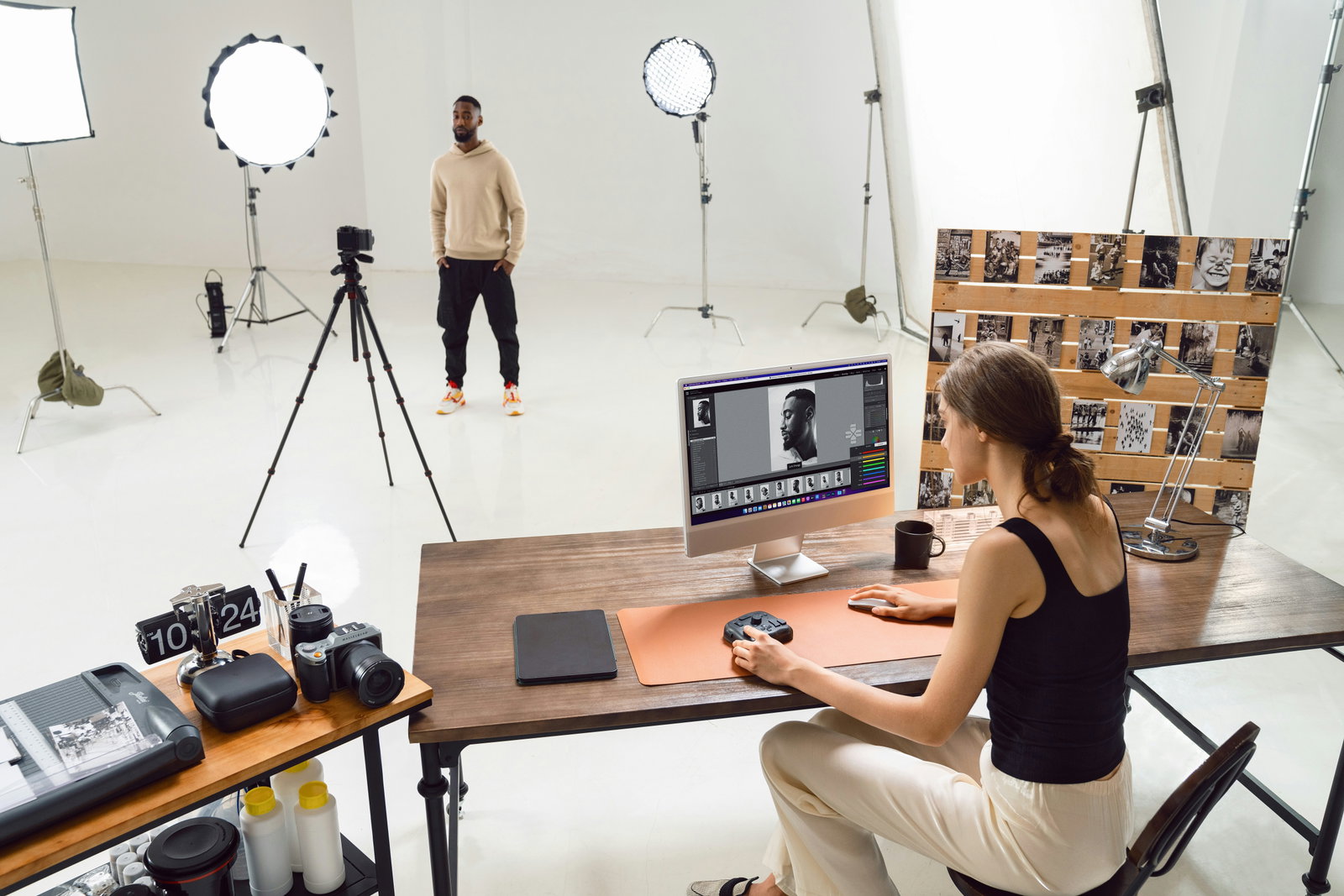 Fotografin sitzt an Schreibtisch und bearbeitet Bilder, Model steht zwischen Softboxen 