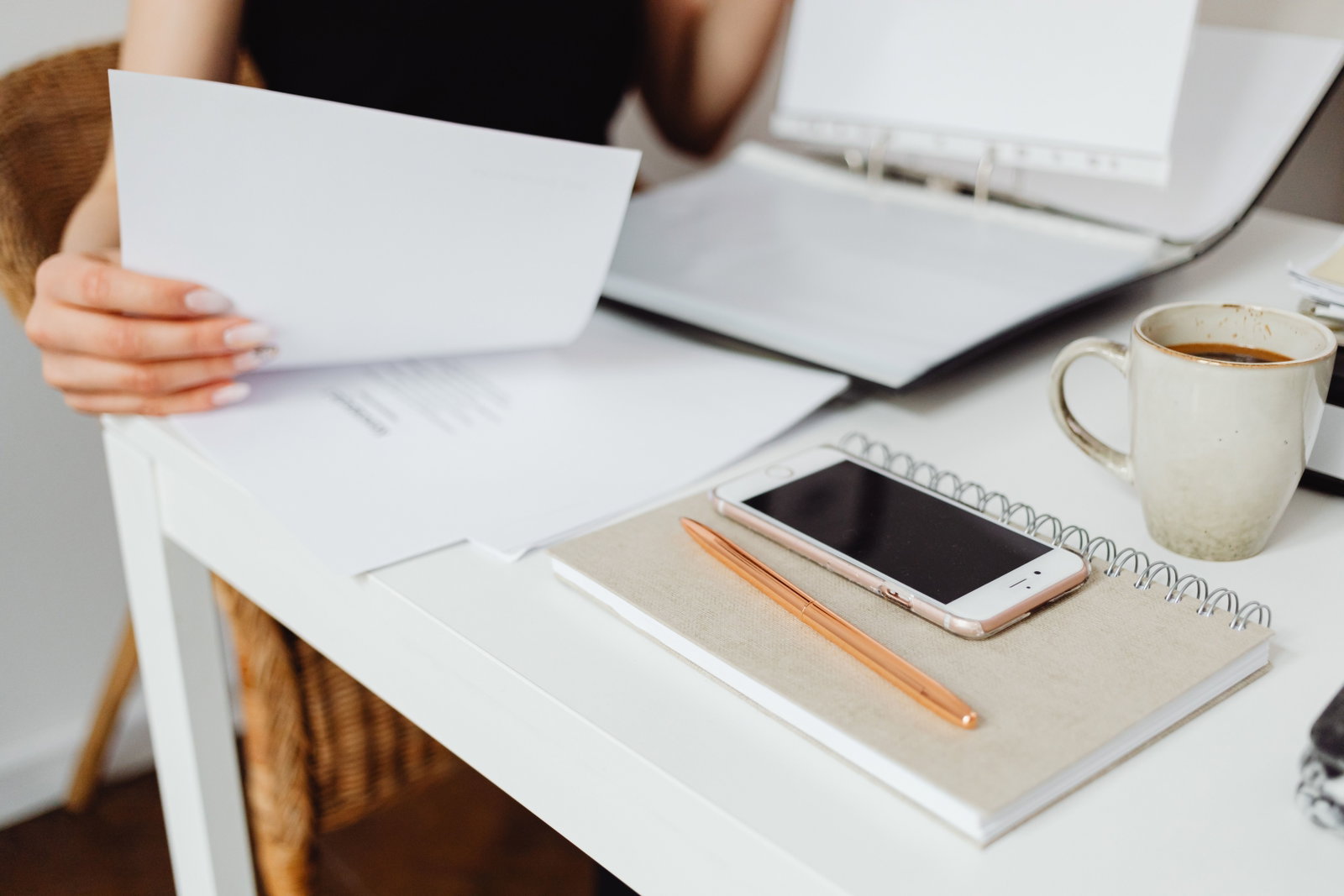 Arbeitsplatz mit Kaffee, Notizbuch, Handy, Stift und Hand die Blätter hält